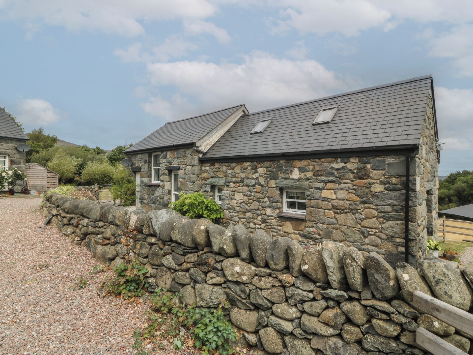 A stone house with a gravel driveway and a stone wall.