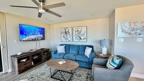 Ein Wohnzimmer mit einem blauen Sofa, einem Couchtisch, einem Fernseher und abstrakter Kunst an der Wand.