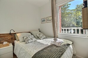Een slaapkamer met een bed, nachtkastjes, een raam met uitzicht en aan de muur hangende foto's.