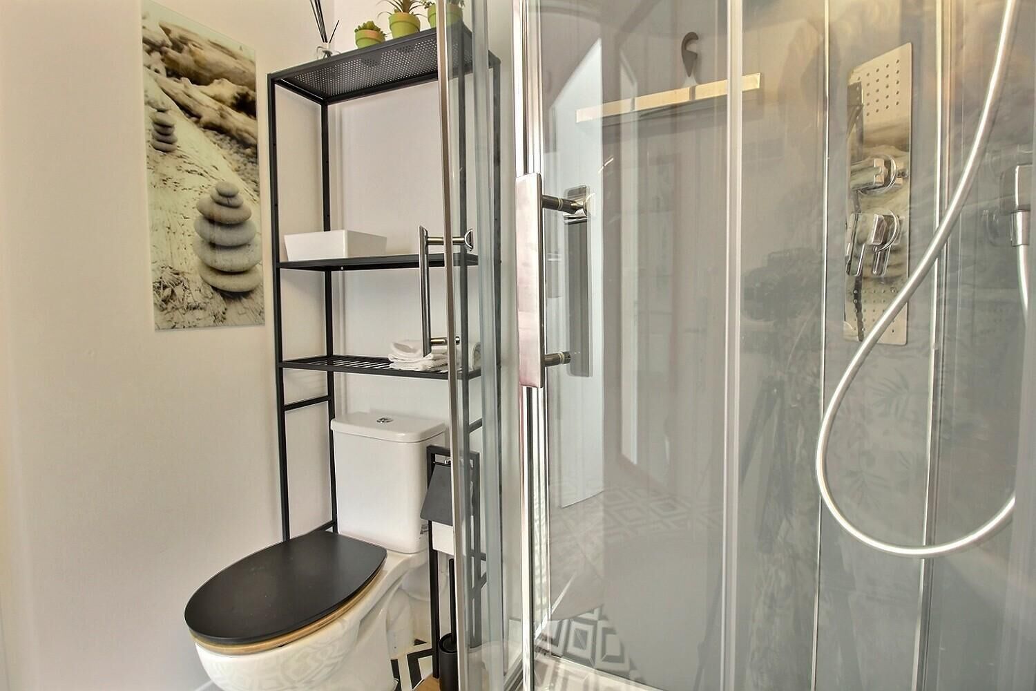 Ein Badezimmer mit einer Duschkabine aus Glas, einer Toilette mit schwarzem Sitz und einem weißen Waschbecken mit schwarzer Arbeitsplatte.