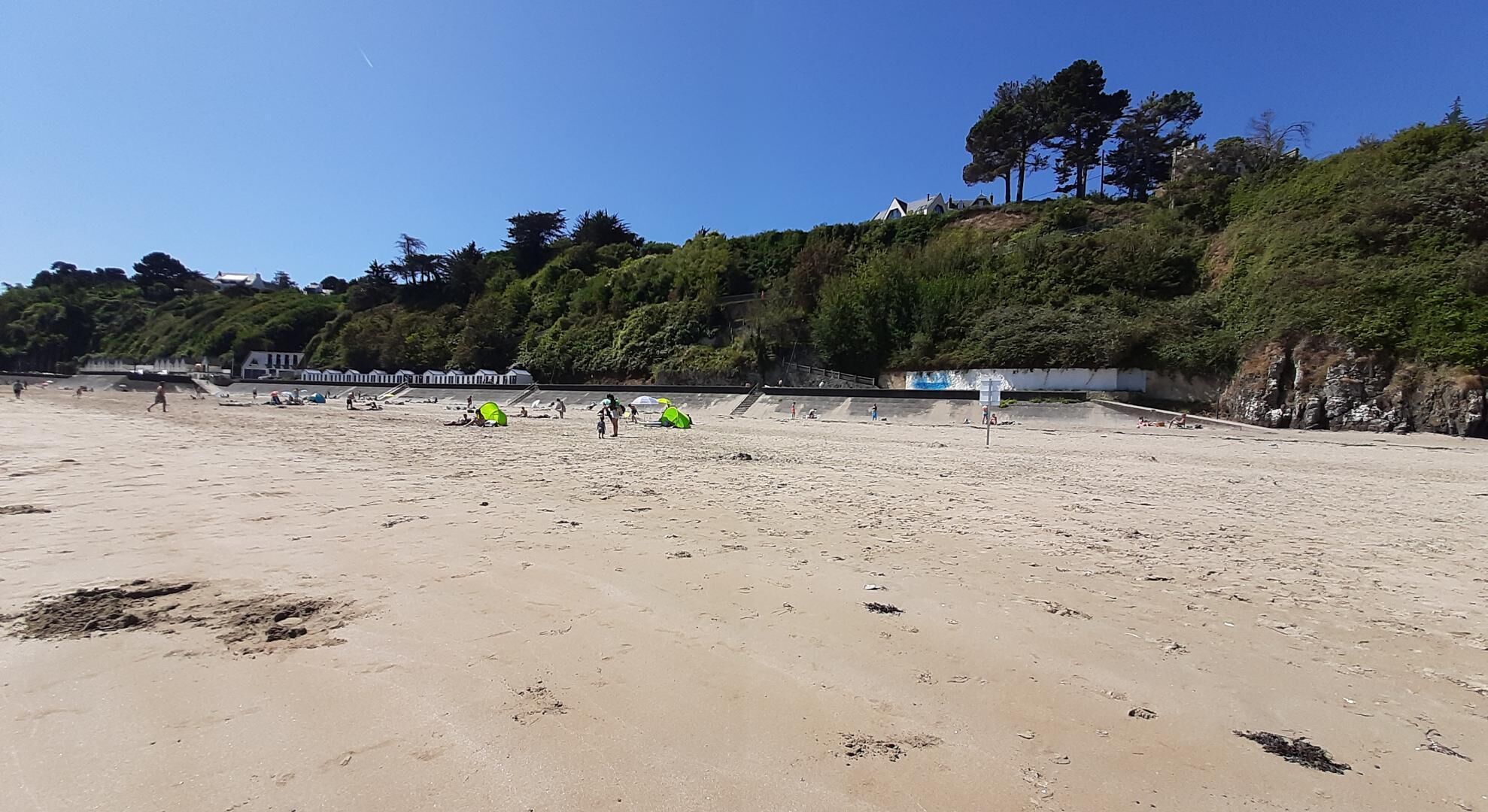 Une plage de sable avec des empreintes de pas, une tente verte et quelques personnes.