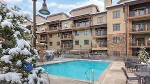 A multi-story hotel with a swimming pool, outdoor seating, and snow-covered trees.