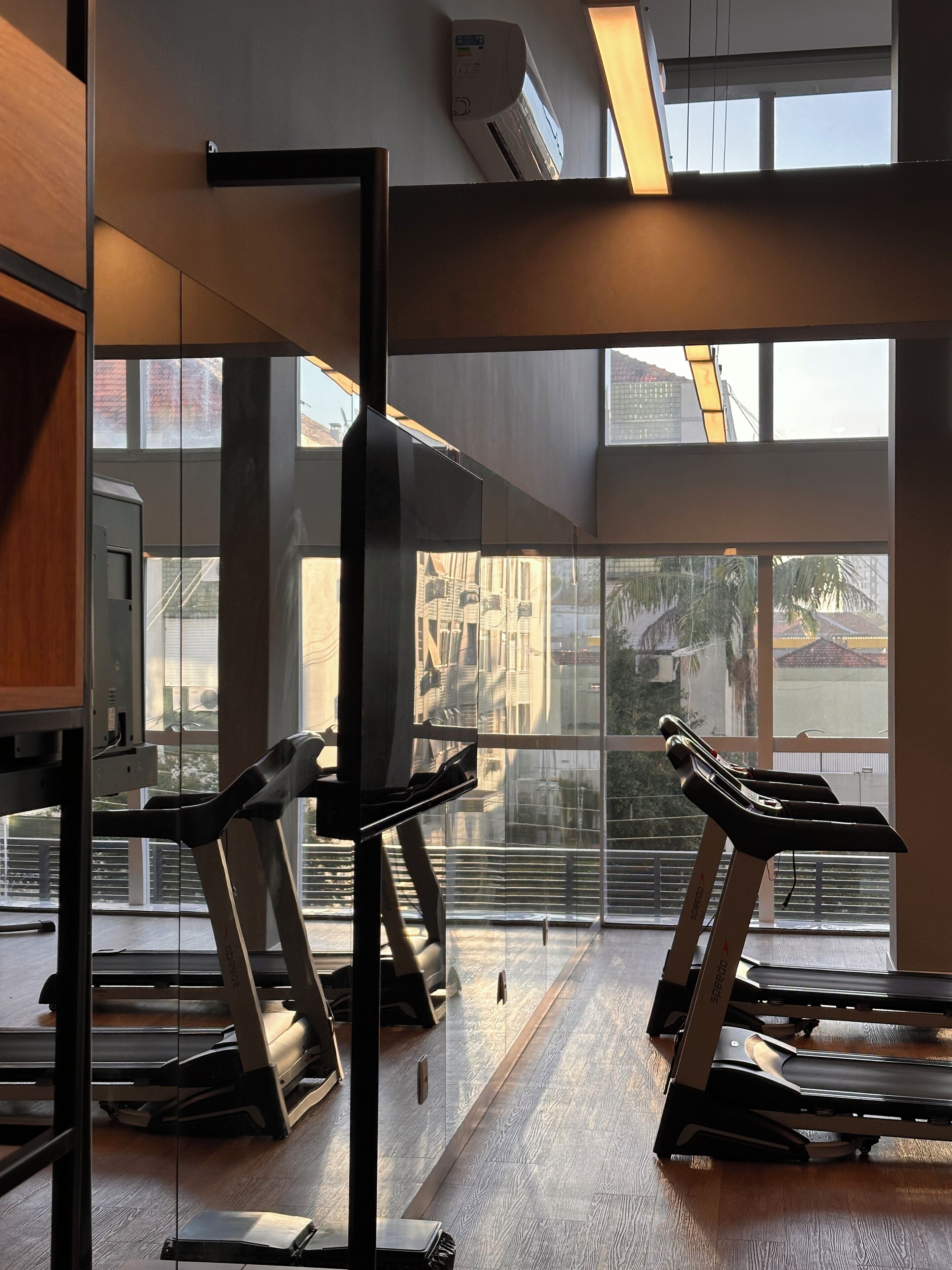 Un gimnasio con cintas de correr, un ventanal grande y un equipo de aire acondicionado.