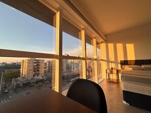 A hotel room with a large window, a bed, a desk, and a chair.