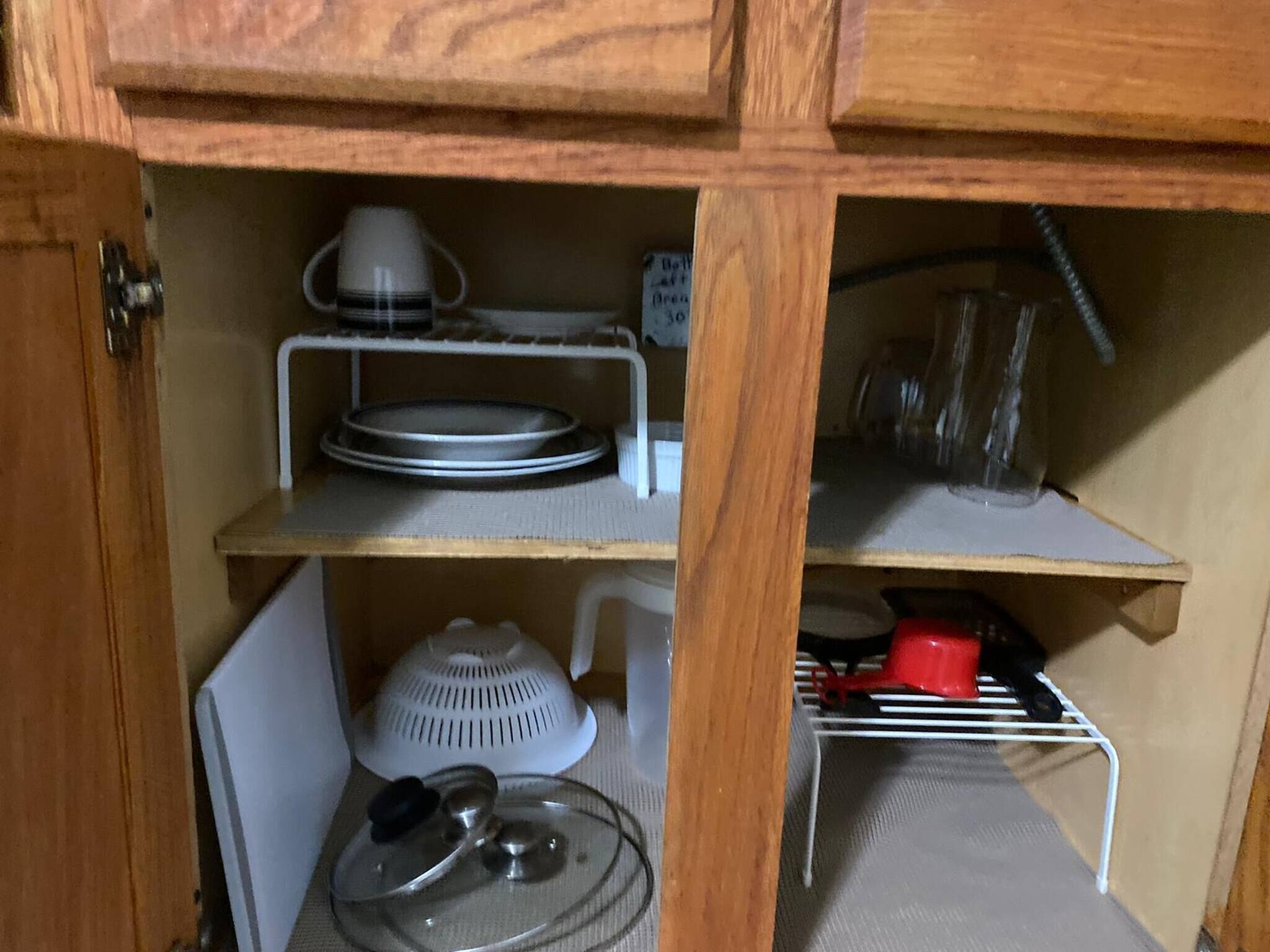 A kitchen cabinet with shelves holding dishes, a kettle, and a red pot.