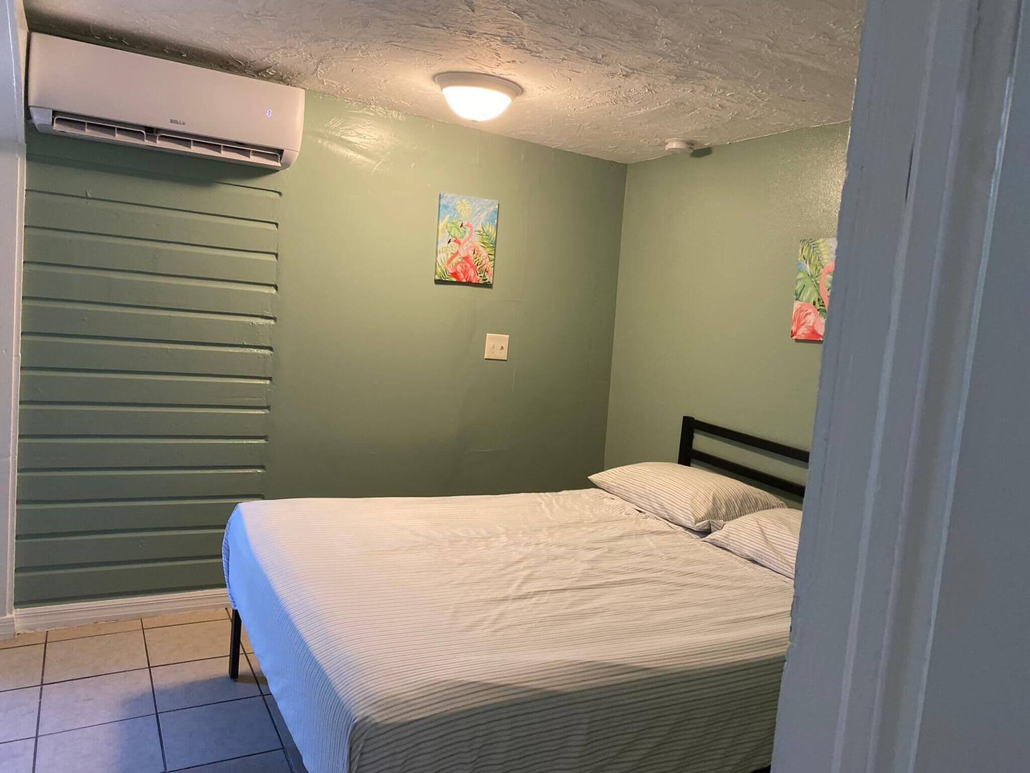 A bedroom with a bed, an air conditioning unit, and two wall-mounted paintings.