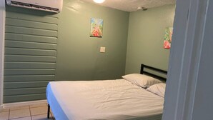 Quarto com cama, ar condicionado e duas pinturas penduradas na parede.