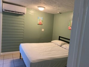 A bedroom with a bed, an air conditioning unit, and two wall-mounted paintings. - Apt 1br, Playgrnd, SRQ Dwntwn, Siesta Key, 20, 3ppl (Sarasota)