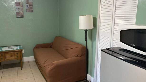 Um quarto com um sofá marrom, uma luminária, um rádio antigo e uma pequena mesa de madeira.