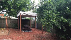 Um quintal com pérgola de madeira, mesa de piquenique e área de estar coberta.