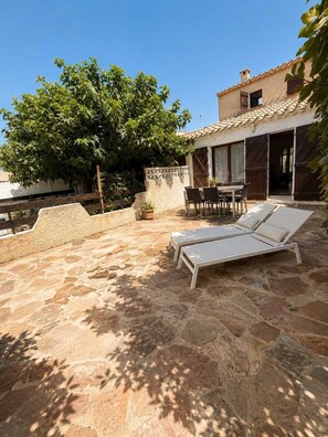 A stone patio with lounge chairs and a table, a wooden fence, and a building with a tiled roof. - Mediterranean villa   Walking distance to the beach 2 terraces (Vendres)