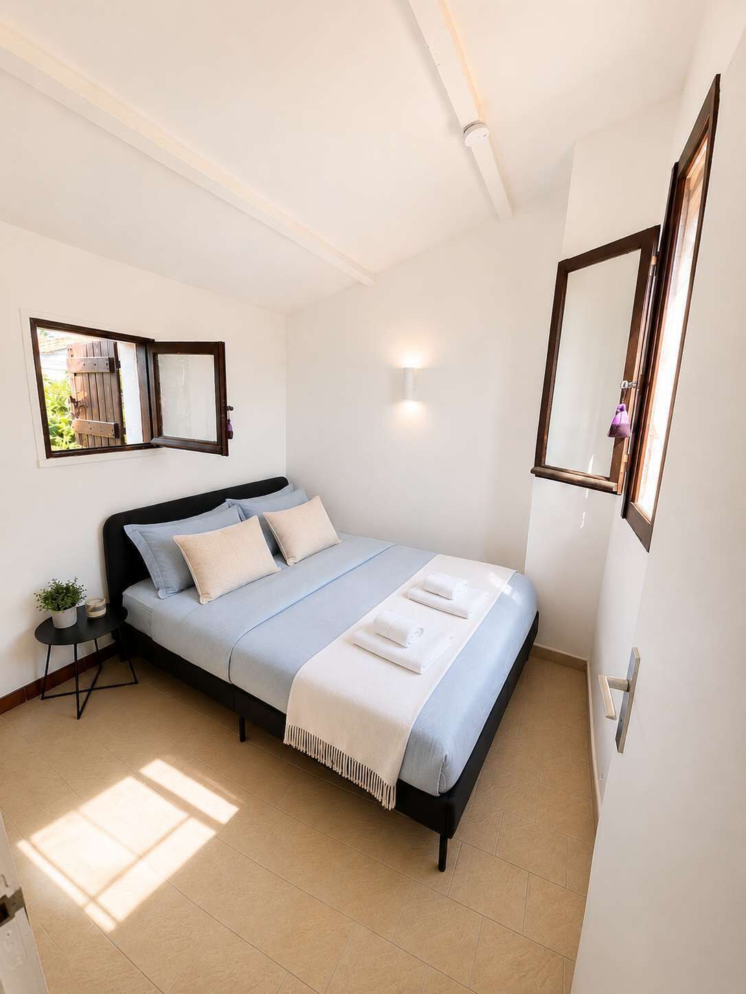 A bedroom with a bed, bedside tables, a wall-mounted mirror, and a window with a view.