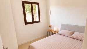 Ein Schlafzimmer mit einem Bett, einem Fenster, einem Nachttisch mit Lampe und einer Tür.