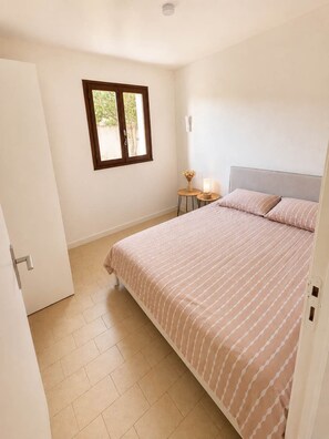 A bedroom with a bed, a window, a bedside table with a lamp, and a door. - Mediterranean villa – Walking distance to the beach – 2 terraces (Vendres)