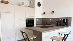A modern kitchen with white cabinets, a Bosch oven, a sink, a coffee maker, and two bar stools. - Valras- Loc Archipel Panarea  vue mer (Valras-Plage)