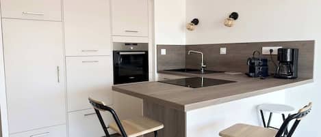 A modern kitchen with white cabinets, a Bosch oven, a sink, a coffee maker, and two bar stools.