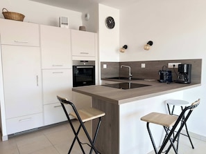Eine moderne Küche mit weißen Schränken, einem Bosch-Backofen, einer Spüle, einer Kaffeemaschine und zwei Barhocker.