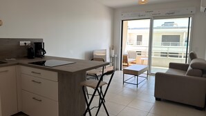 A modern kitchen with a built-in stove, a coffee maker, and a dining area with a table and chairs. - Valras- Loc Archipel Panarea  vue mer (Valras-Plage)