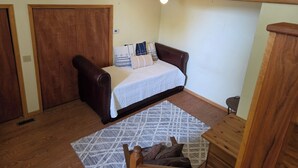 Quarto com cama, guarda-roupa de madeira, pequena mesa de madeira e tapete estampado.