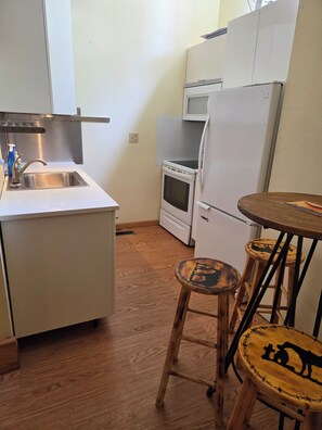 A compact kitchen with a sink, stove, and microwave. There are two stools with animal designs. - Cozy loft apartment in historic downtown Cole Camp. (Cole Camp)