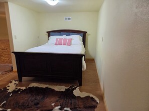 Un dormitorio con cama de madera, ropa de cama blanca y alfombra de cuero.