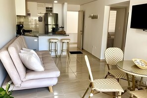Ein Wohnzimmer mit einer Couch, zwei Stühlen, einem Esstisch und einer Küchenzeile im Hintergrund.