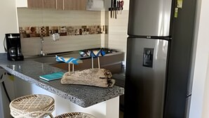 A kitchen with a stainless steel refrigerator, a coffee maker, and two wicker bar stools. - Rodadero Relax | Walk to Beach & Park (Santa Marta)