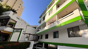 A multi-story residential building with balconies, a gated parking area, and a small garden with red flowers. - Rodadero Relax | Walk to Beach & Park (Santa Marta)