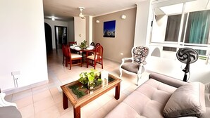 A living room with a sofa, a coffee table with a plant, a dining area with chairs and a table, and a window with curtains. - Enjoy Rodadero 1 Block to Beach | 3BR 3BA Fits 10 (Santa Marta)