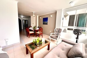 A living room with a sofa, a coffee table with a plant, a dining area with chairs and a table, and a window with curtains. - Enjoy Rodadero 1 Block to Beach | 3BR 3BA Fits 10 (Santa Marta)