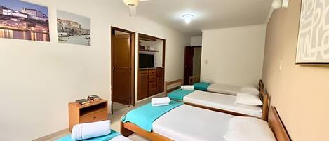 A hotel room with three beds, a ceiling fan, a small table with books, and a wardrobe.