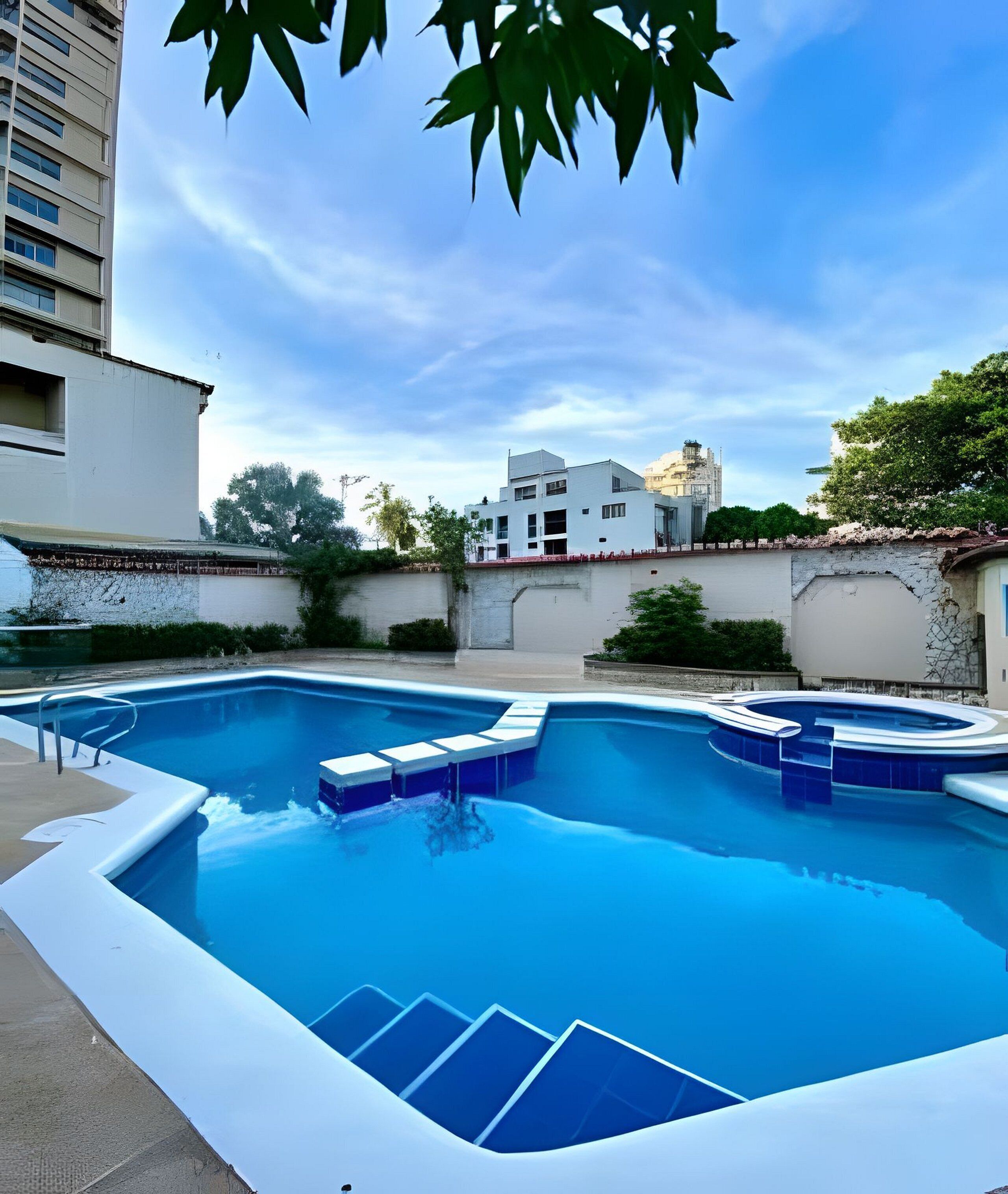 A swimming pool with a modern design, surrounded by a low wall and a building in the background.