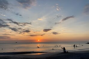 A beach scene with the sun setting over the horizon, people in the water, and a clear sky. - Bello Horizonte Haven | Resort Pools & Beach (Santa Marta)
