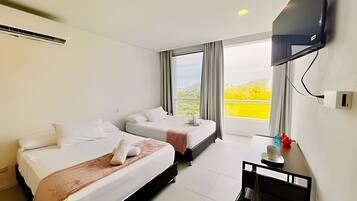 A hotel room with two beds, a flat-screen TV mounted on the wall, and a window with a view of greenery.