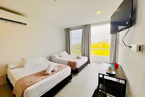 A hotel room with two beds, a flat-screen TV mounted on the wall, and a window with a view of greenery.