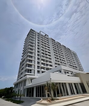 Un immeuble moderne de grande hauteur, doté de nombreux étages et de balcons, et caractérisé par une entrée imposante avec un espace abrité et un jardin aménagé.
