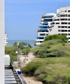 Uma área residencial à beira-mar, com edifícios modernos, céu claro e um caminho que leva à praia.