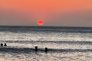 Un coucher de soleil sur l’océan, avec les silhouettes de personnes dans l’eau.