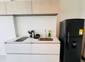 Une cuisine moderne avec des meubles blancs, un réfrigérateur noir et un petit espace dédié à l’évier.