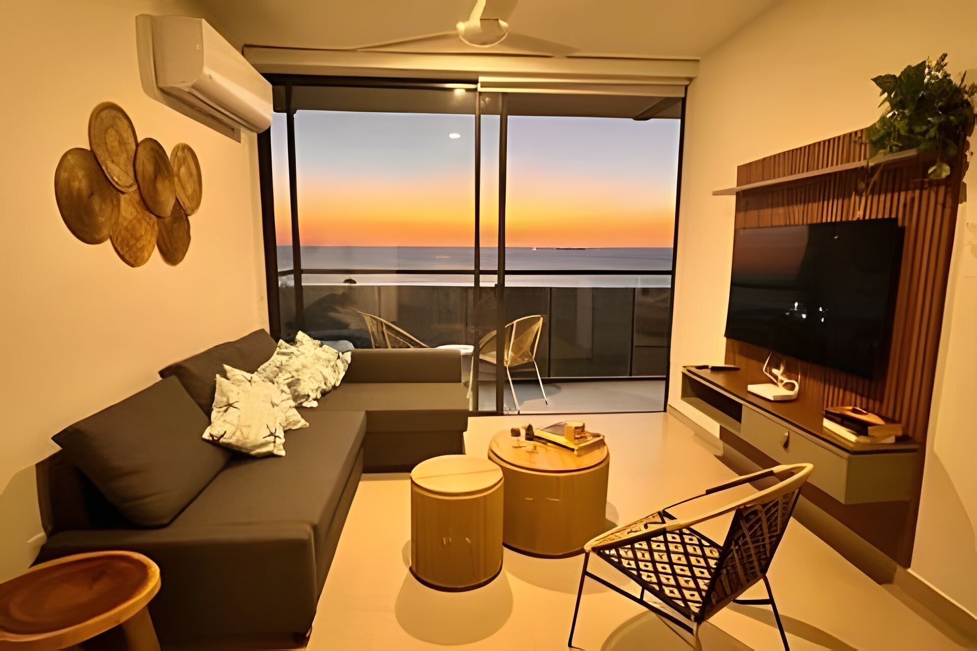 Un salon moderne comprenant un canapé, deux fauteuils, une table basse, un téléviseur et un balcon offrant une vue sur le coucher de soleil.