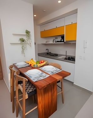 A compact kitchen with modern appliances, a dining table set with plates and cutlery, and a small plant on the wall.