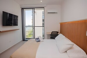 A bedroom with a bed, a desk, a chair, a TV, and a view of the outside. - Ocean view, swimming pools, gym, and beach access (Santa Marta)