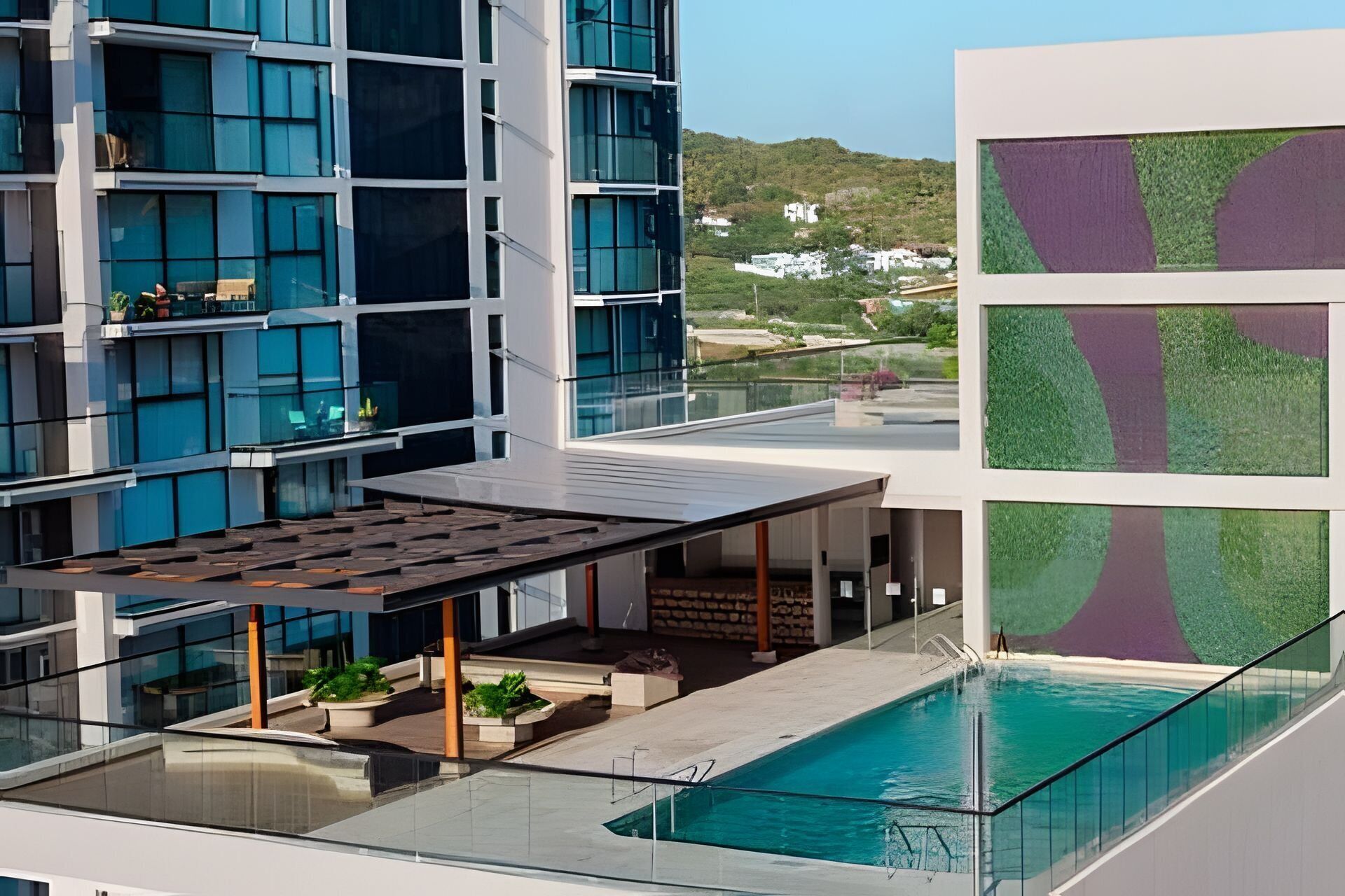 Um hotel moderno com piscina no terraço, guarda-corpos de vidro e vista para a paisagem ao redor.