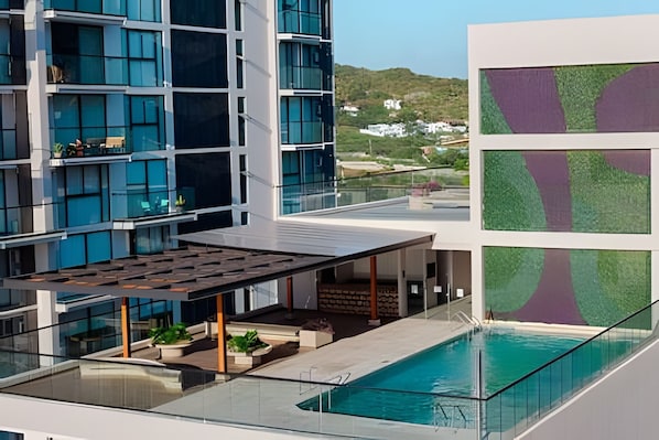 A modern hotel with a rooftop pool, glass railings, and a view of the surrounding landscape.