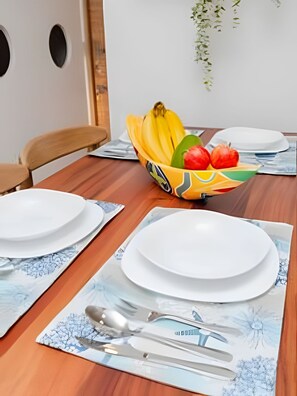 A dining table set with white plates, a bowl of fruit, and placemats with a tree design. - Ocean view, swimming pools, gym, and beach access (Santa Marta)