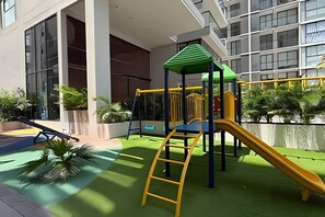 An outdoor play area with a slide and climbing structures, surrounded by a building with large windows and a paved walkway. - Ocean View Loft, Gym, Pozos Colorados (Santa Marta)