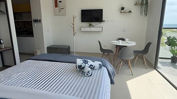 Et moderne hotelværelse med en seng, et fjernsyn, et lille bord med stole og en balkon med planter.
