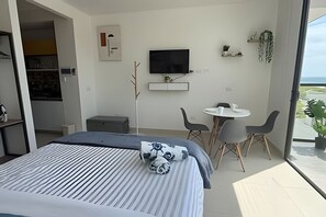 A modern hotel room with a bed, a TV, a small table with chairs, and a balcony with plants. - Ocean View Loft, Gym, Pozos Colorados (Santa Marta)