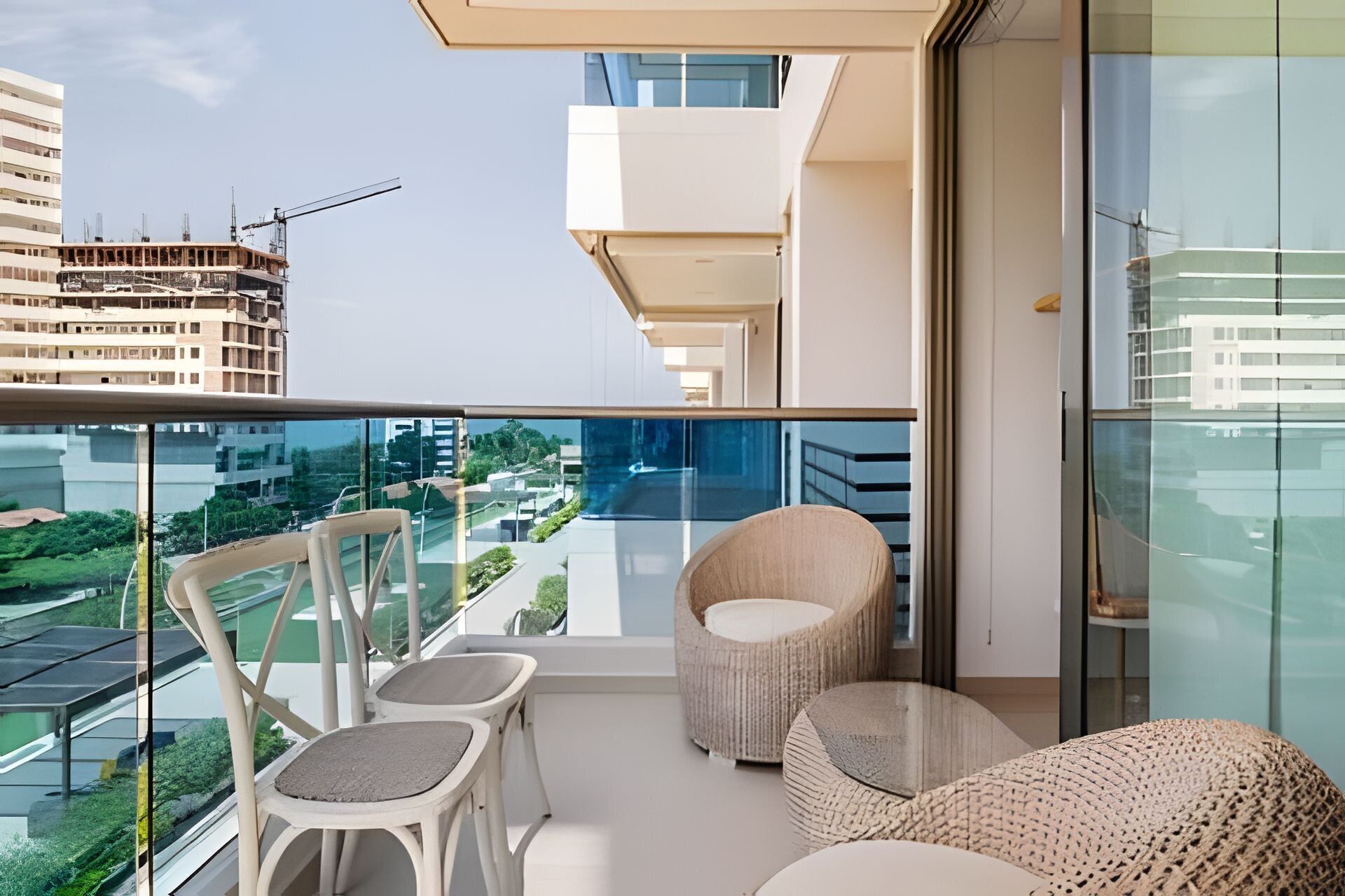 A balcony with a glass railing, two wicker chairs, and a round woven ottoman.