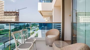 A balcony with a glass railing, two wicker chairs, and a round woven ottoman.